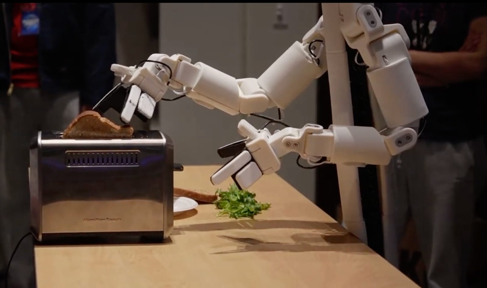 A pair of robot arms placing bread into a toaster on a demo table.