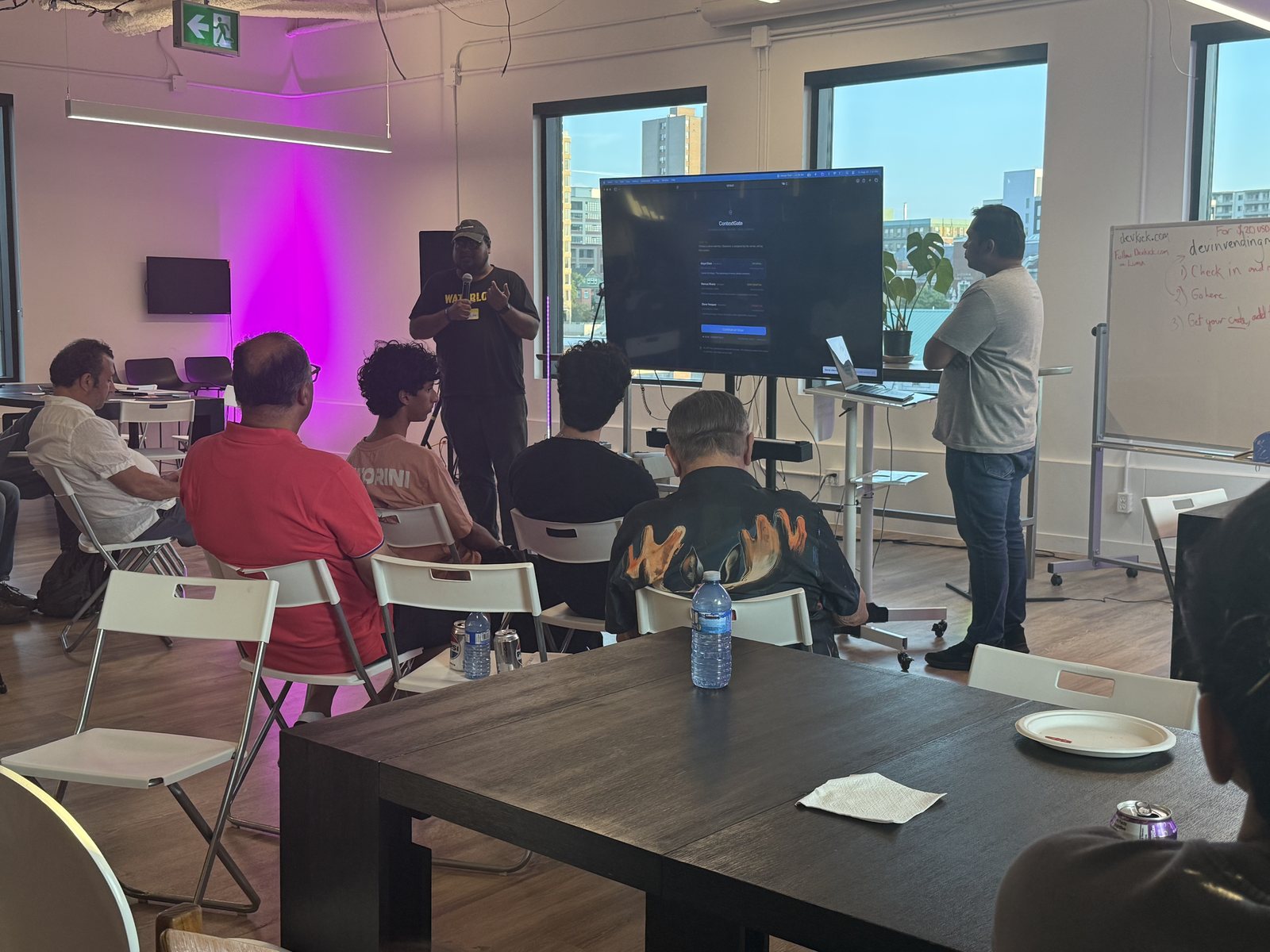 Presenter addressing a seated audience at devkick Kick 002, with a live demo on the room's main screen