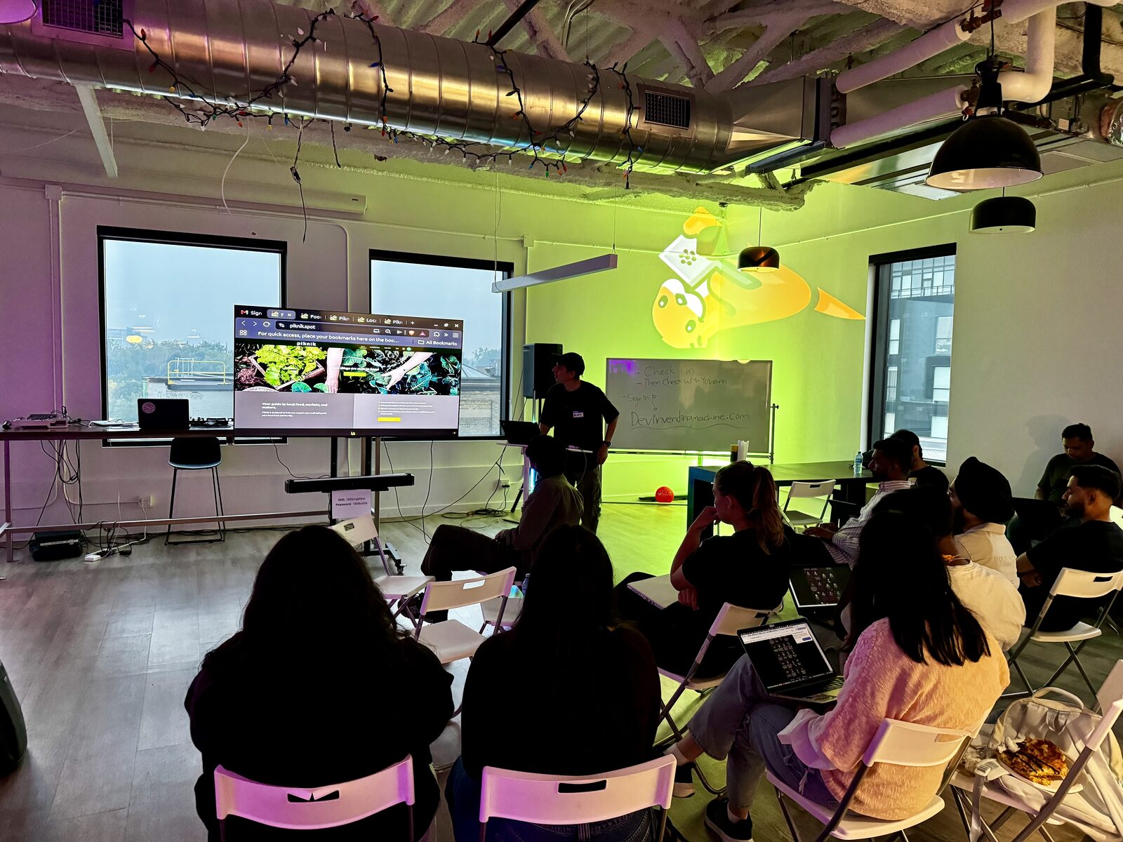 A builder demoing a project on the big screen to the room under green light