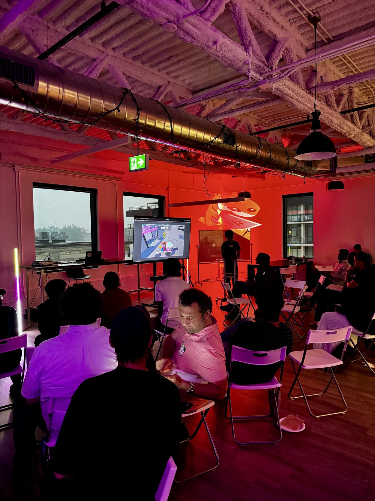 Attendees watching a live game demo on screen under red light